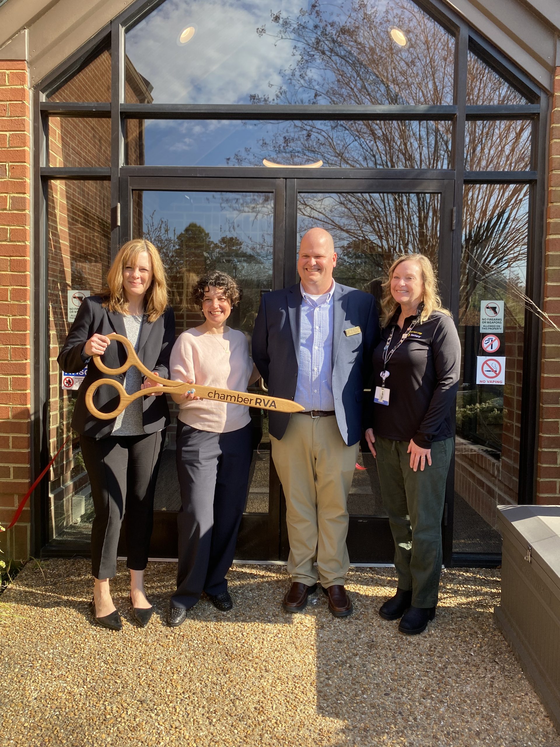 Four tenants of the Commonwealth Autism All Abilities Inclusion and Innovation Center hold a pair of ceremonial wooden scissors in front of doors at a ribbon cutting for the building in Richmond, Virginia.